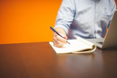 Man writing on pad with laptop